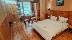 A wooden-floored bedroom with a bed, bedside tables, a small table, and a chair. - Tirthan Riverside Cottage (Banjar)