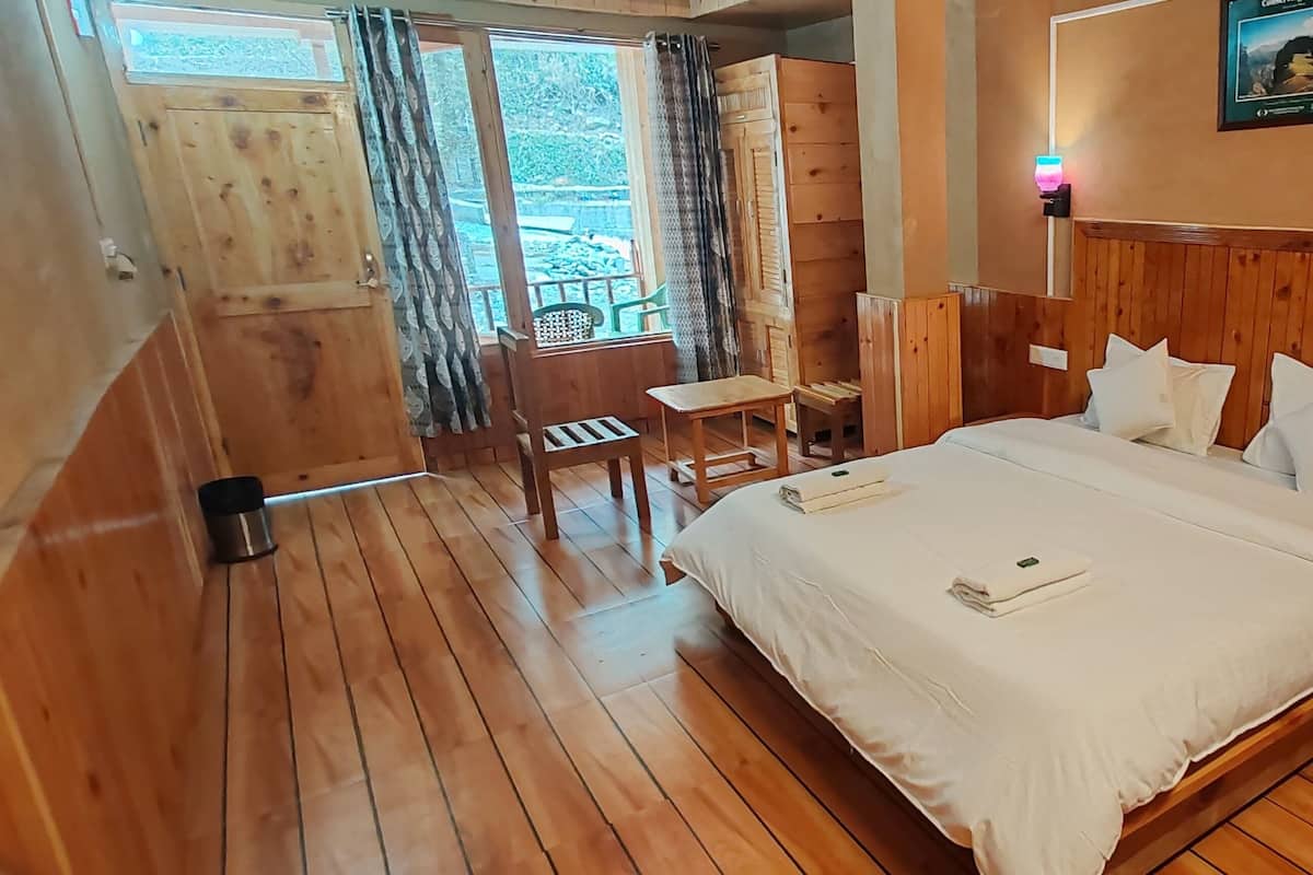 A wooden-floored bedroom with a bed, bedside tables, a small table, and a chair.