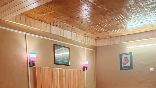 A wooden-paneled room with a bed, bedside table, and wall-mounted lamp. - Tirthan Riverside Cottage (Banjar)