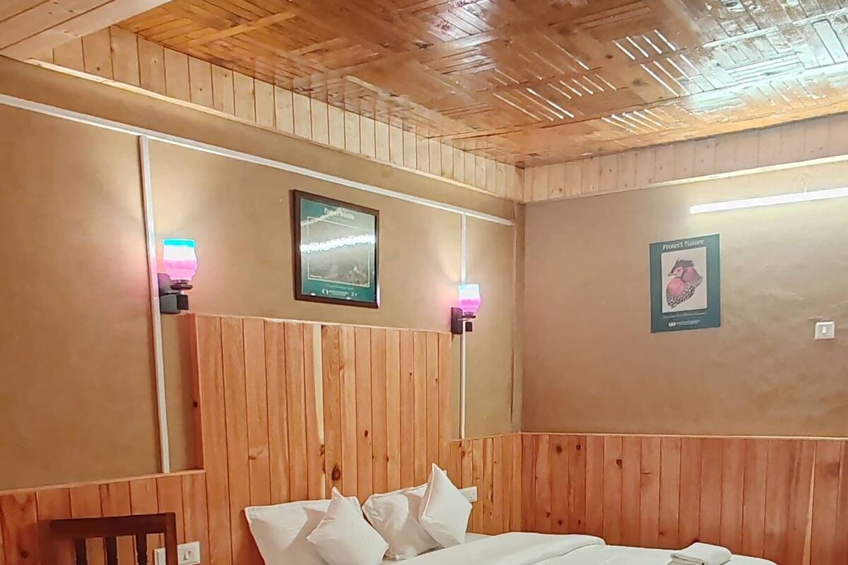 A wooden-paneled room with a bed, bedside table, and wall-mounted lamp.