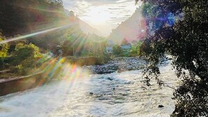 A river flowing through a valley with mountains on either side and a clear sky above. - Tirthan Riverside Cottage (Banjar)