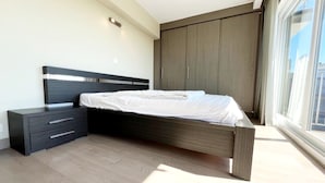 Ein modernes Schlafzimmer mit Bett, Nachttisch, Kleiderschrank und einem großen Fenster.