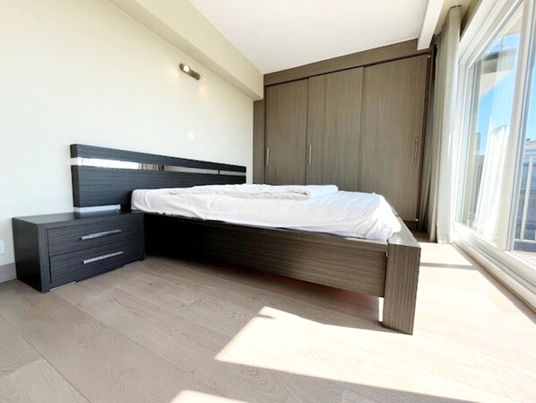 Un dormitorio moderno con cama, mesita de noche, armario y un ventanal grande.
