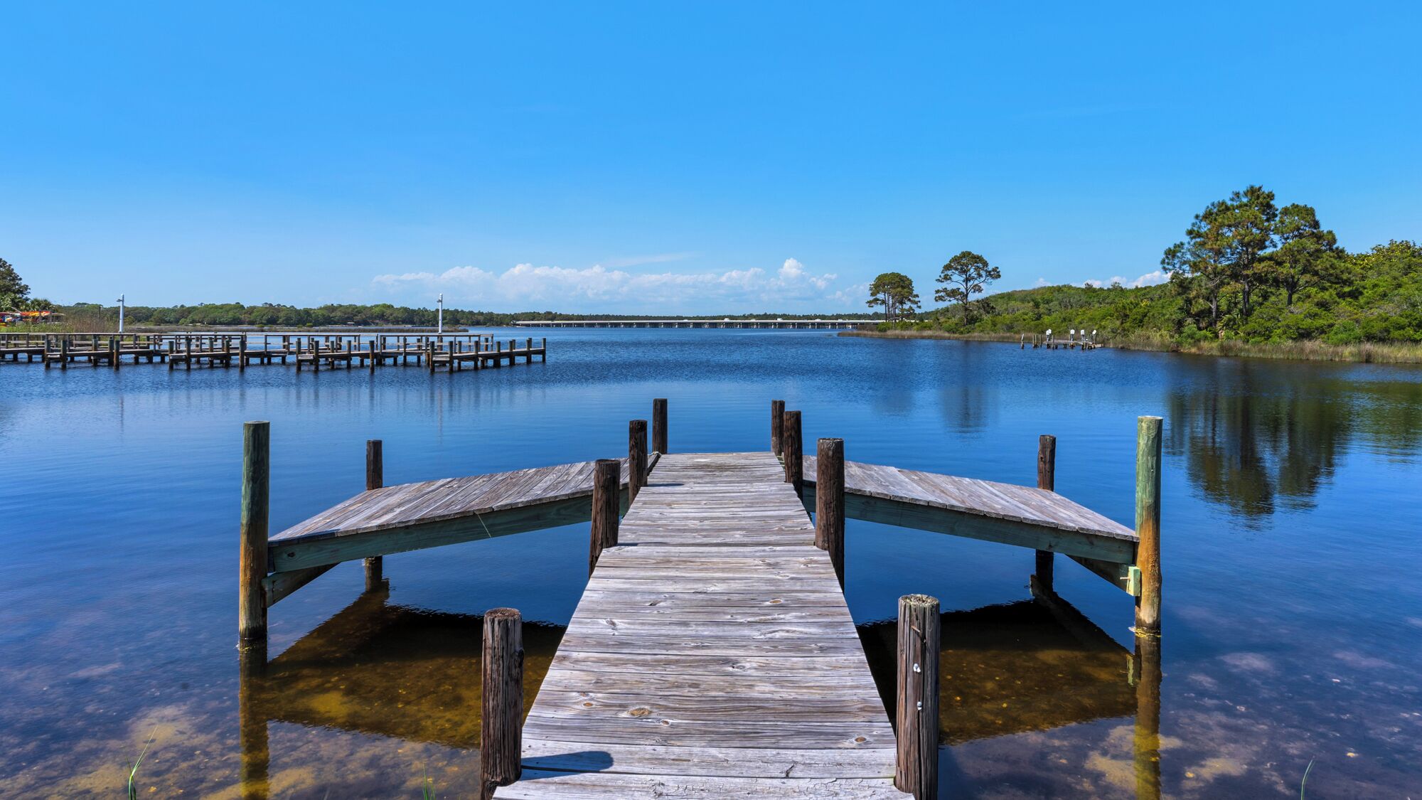 A wooden pier extending into calm water with a clear sky above.