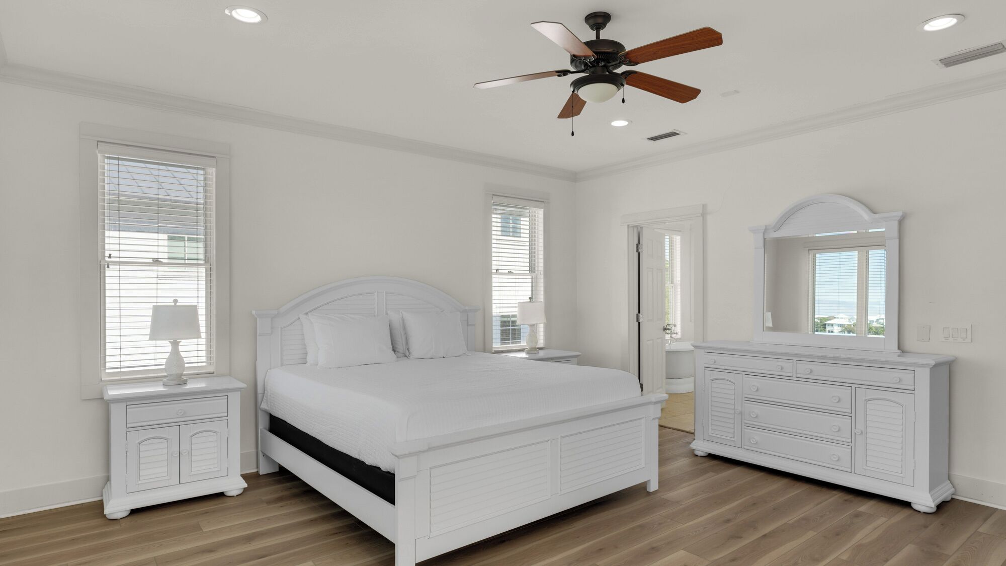 A bedroom with a bed, a dresser, a mirror, and a ceiling fan.