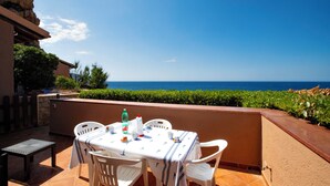 Mesa al aire libre con vista al mar, rodeada de sillas blancas y un mantel con motivos náuticos.