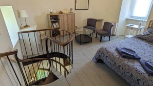 Un dormitorio con una cama, un escritorio, dos sillas, una mesa redonda pequeña, una estantería y una escalera.
