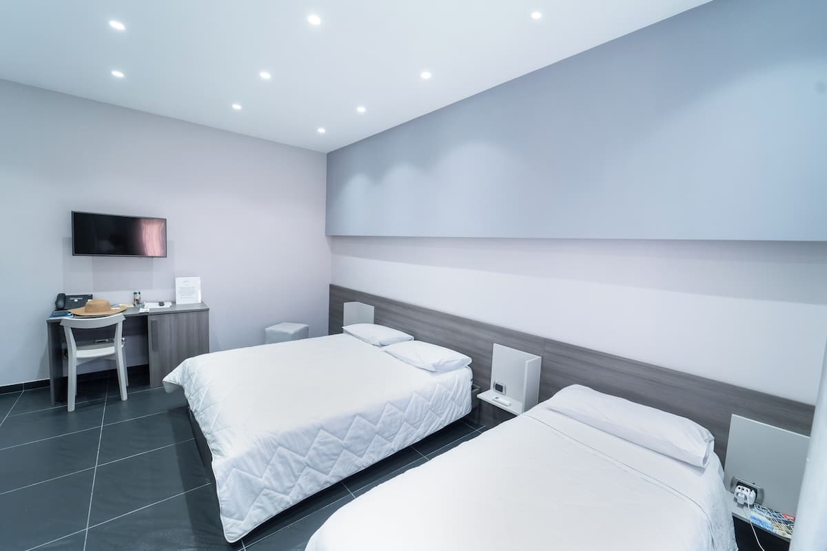 A modern hotel room with two beds, a desk, a flat-screen TV, and a bedside table with a lamp.