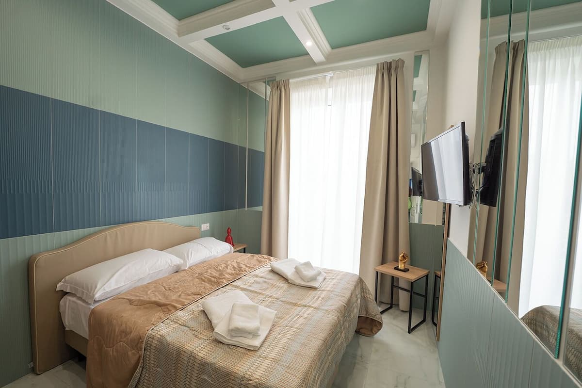 A hotel room with a bed, a TV, a small table, and a mirror.