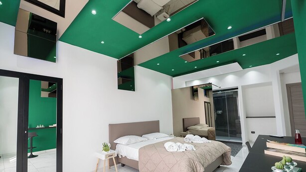 A modern hotel room with a large bed, a separate shower area, and a dining table with books and a cactus. - GREROS H. PORTO NAPOLI CENTRO by ClaPa Group Dislocated Hospitality (Naples)