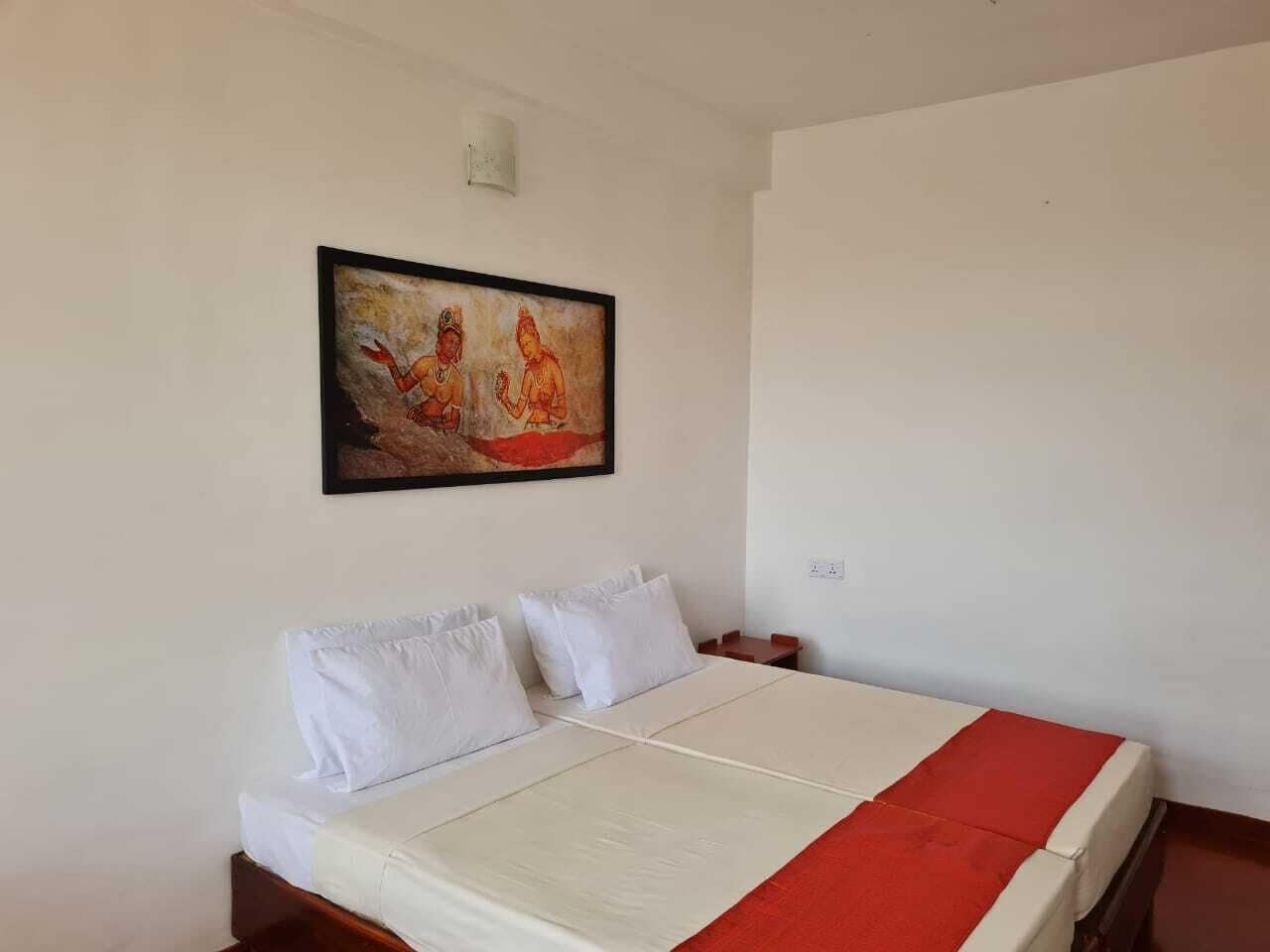 Een hotelkamer met een bed, witte kussens, een rode deken en een schilderij aan de muur.