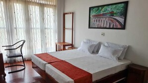Un lit double avec un couvre-lit rouge, une table de chevet en bois, une chaise et un tableau accroché au mur.