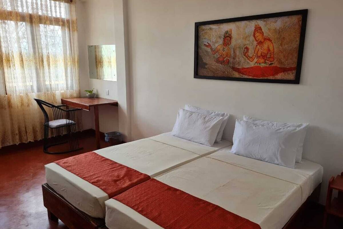 A double bed with white and red bedding, a desk with a chair, and a painting on the wall.