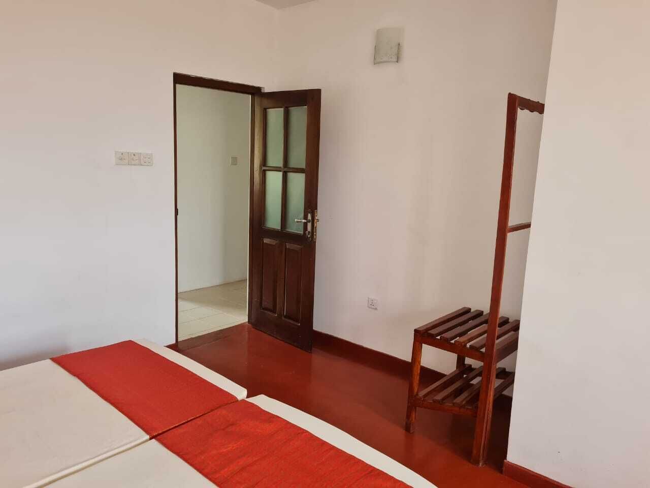 Una habitación con una puerta de madera, un pequeño estante de madera y un tapete rojo y blanco en el suelo.