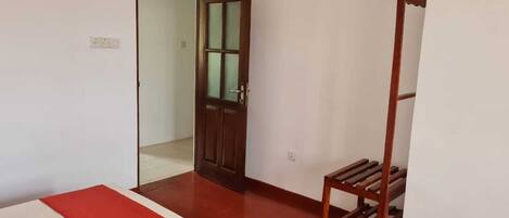 A room with a wooden door, a small wooden shelf, and a red and white mat on the floor.