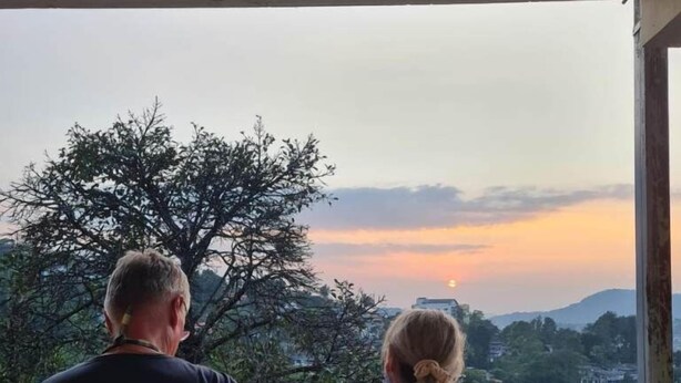 Deux personnes se tiennent sur un balcon, d  ’où elles peuvent admirer un magnifique panorama sur la ville et les montagnes au coucher du soleil.