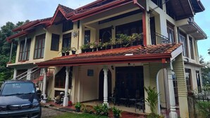 Une maison à deux étages, avec un toit recouvert de tuiles rouges, plusieurs balcons et un jardin agrémenté de plantes en pot.