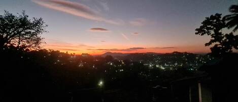 A nighttime view of a cityscape with a sunset or sunrise, featuring distant city lights and a clear sky.