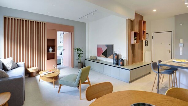A modern living room with a sofa, coffee table, and chairs. There is a kitchen area with a dining table and chairs.