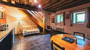 A cozy room with a wooden ceiling, a bed, a table with chairs, and a staircase. - 1BDR Apt + Sofa Bed w/ Garden + Jacuzzi (Étivey)