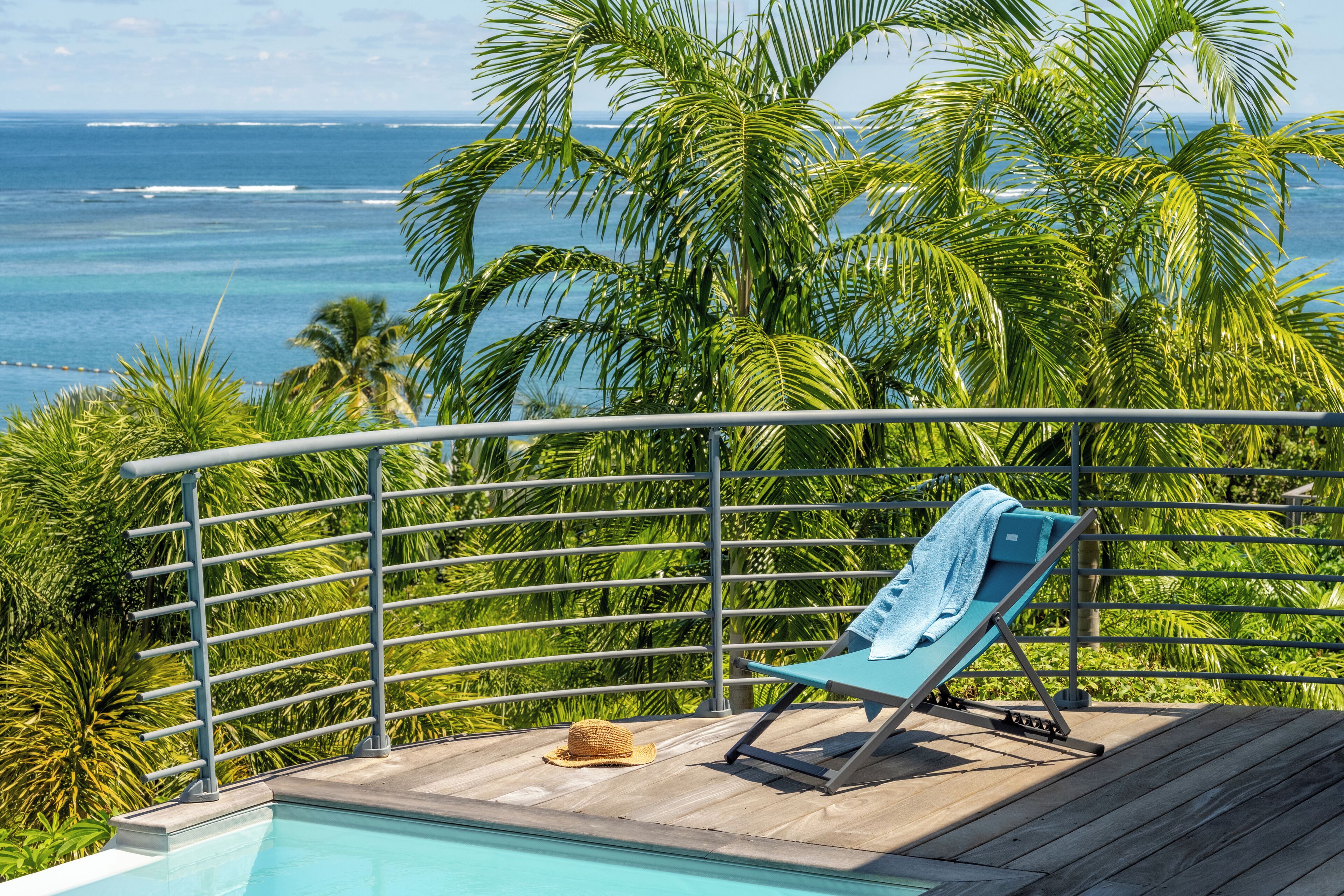 Ein Poolbereich mit Blick auf das Meer, eine Liege und ein Hut auf dem Deck.