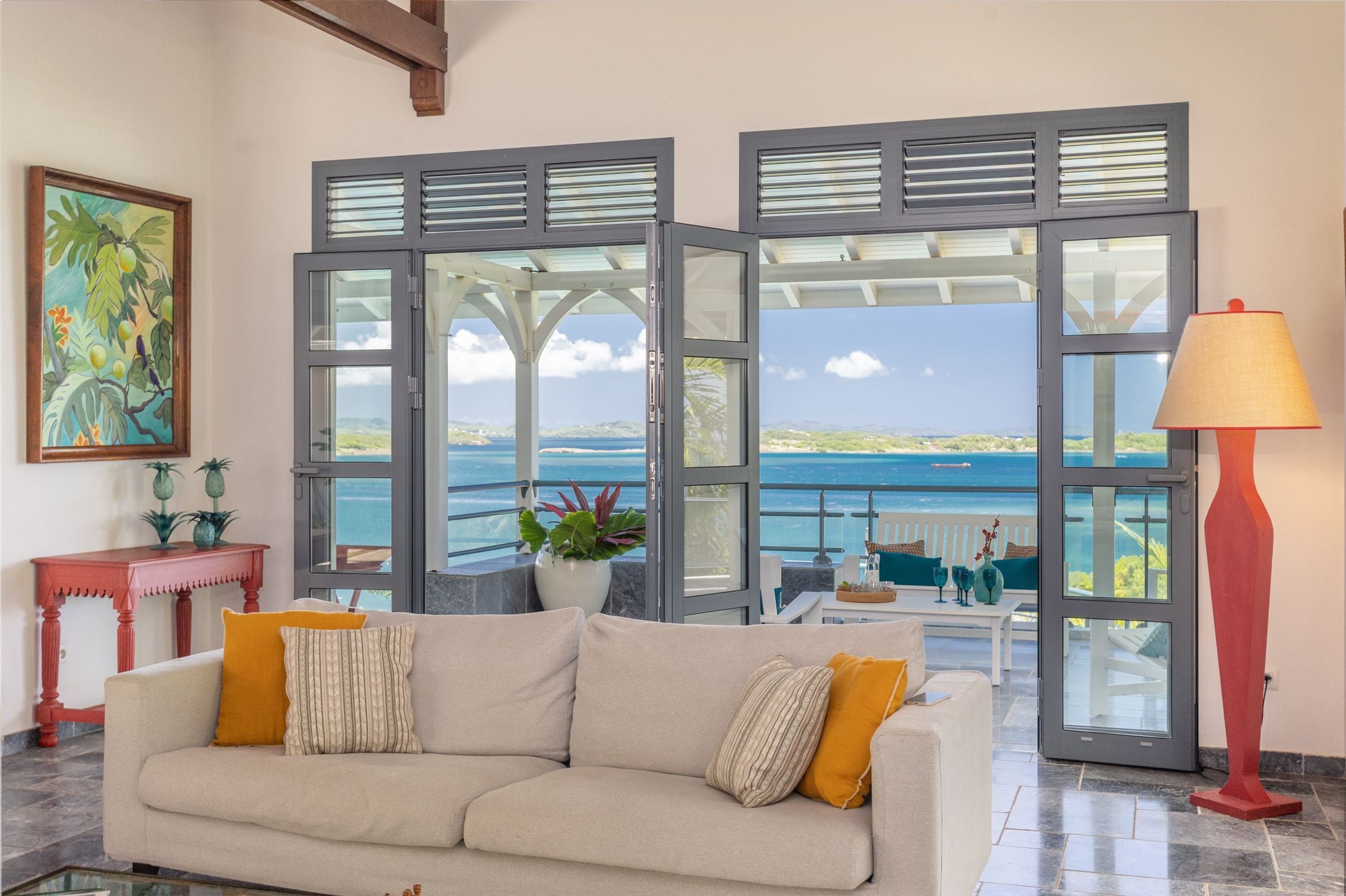 Una sala de estar con sofá, una mesa y vista al mar a través de amplios ventanales.