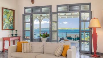 A living room with a sofa, a table, and a view of the sea through large windows.