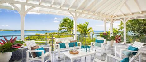 An outdoor patio with white furniture and a view of the ocean.