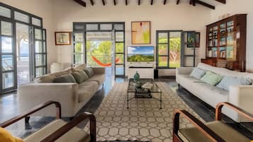 A spacious living room with two sofas, a coffee table, and a bookshelf. Large windows offer a view of the outdoors.