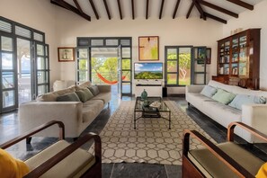 A spacious living room with two sofas, a coffee table, and a bookshelf. Large windows offer a view of the outdoors. - Villa Big Blue  (Le François)