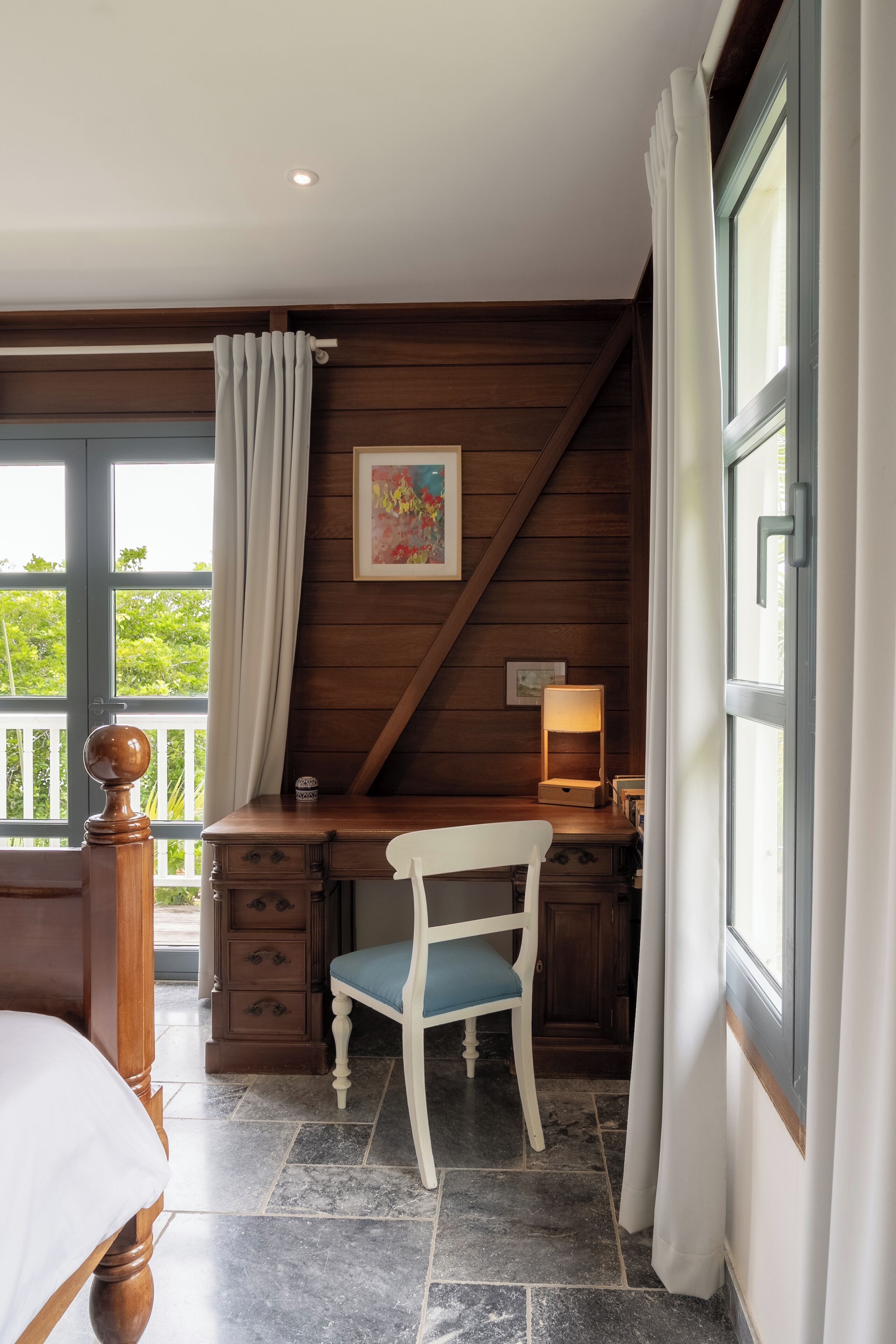Une chambre à coucher avec un lit, un bureau avec une chaise, une fenêtre avec des rideaux et une vue sur la verdure à l’extérieur.