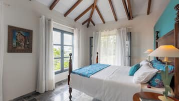 A bedroom with a bed, curtains, a window, a painting, and a nightstand with a lamp.