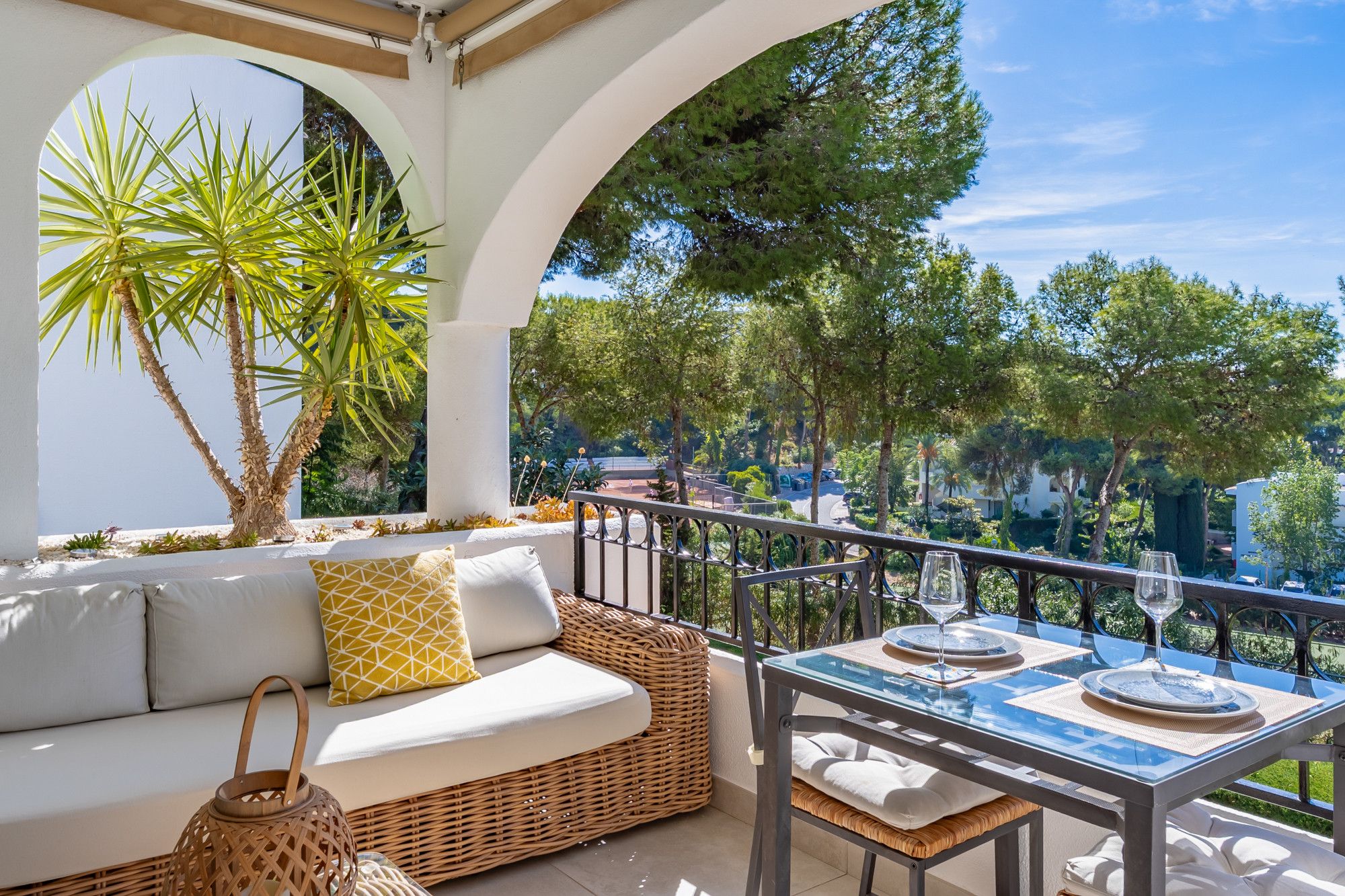 A balcony with a sofa, table set for dining, and a wicker basket.
