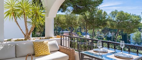 A balcony with a sofa, table set for dining, and a wicker basket.