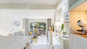 A modern hotel room with a bed, a desk, a chair, a balcony with a view, and a window with curtains. - Spacious studio apartment in Miraflores (Mijas Costa)