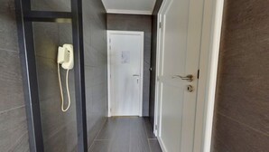 A narrow hallway with a telephone on the left, a door at the end, and a door with a lock on the right.