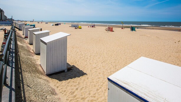 A beach with portable beach huts, a sandy shore, and a clear blue sky.