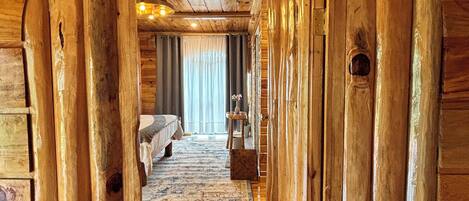 A wooden hallway leading to a bedroom with a bed, a small table, and a chair.