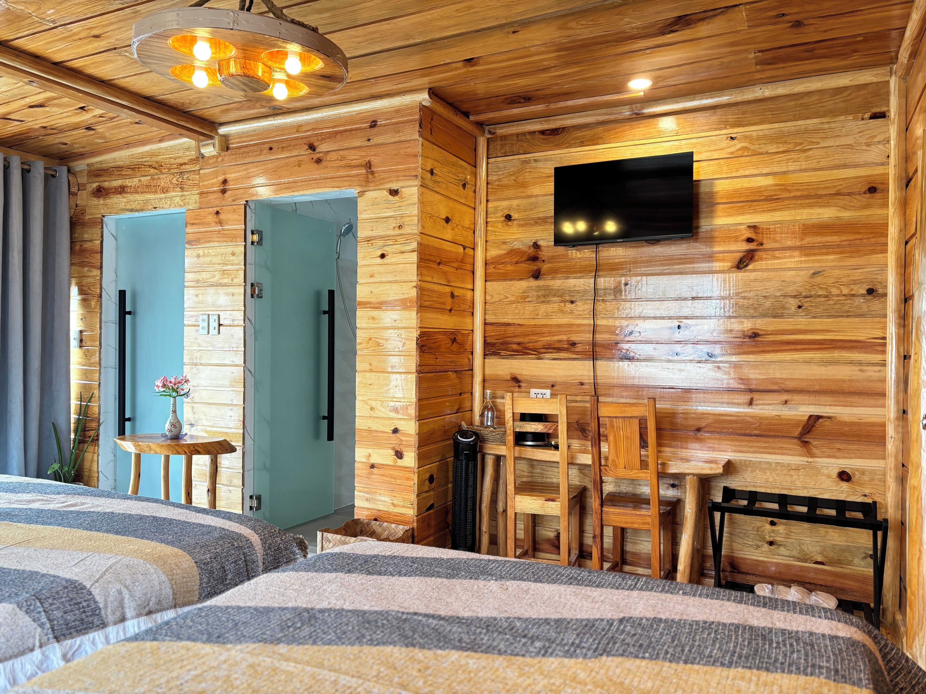 Habitación de cabaña de madera con dos camas, un televisor y una mesita con un florero.