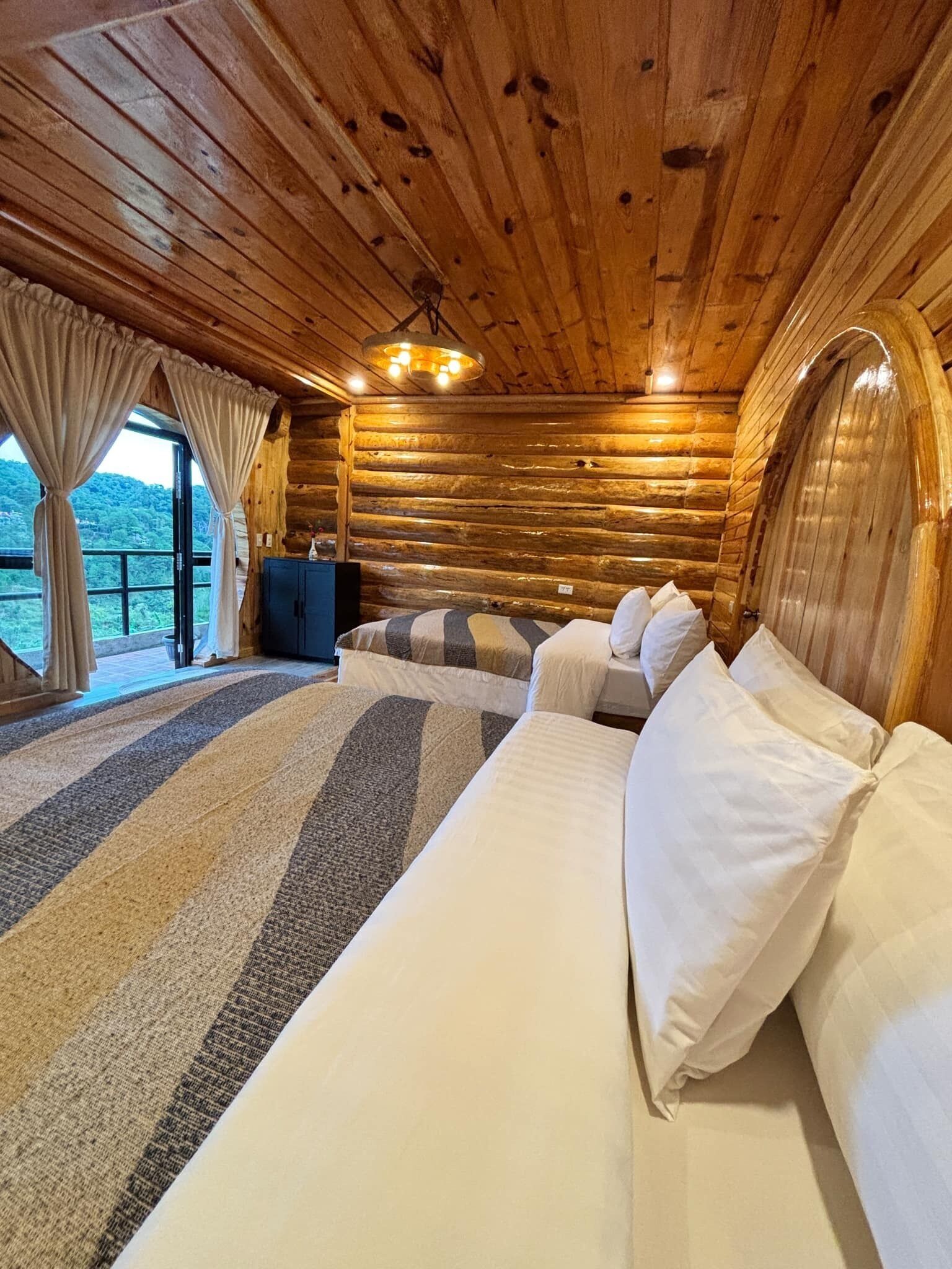 A log cabin bedroom with a large bed, a dresser, and a view of the outdoors.