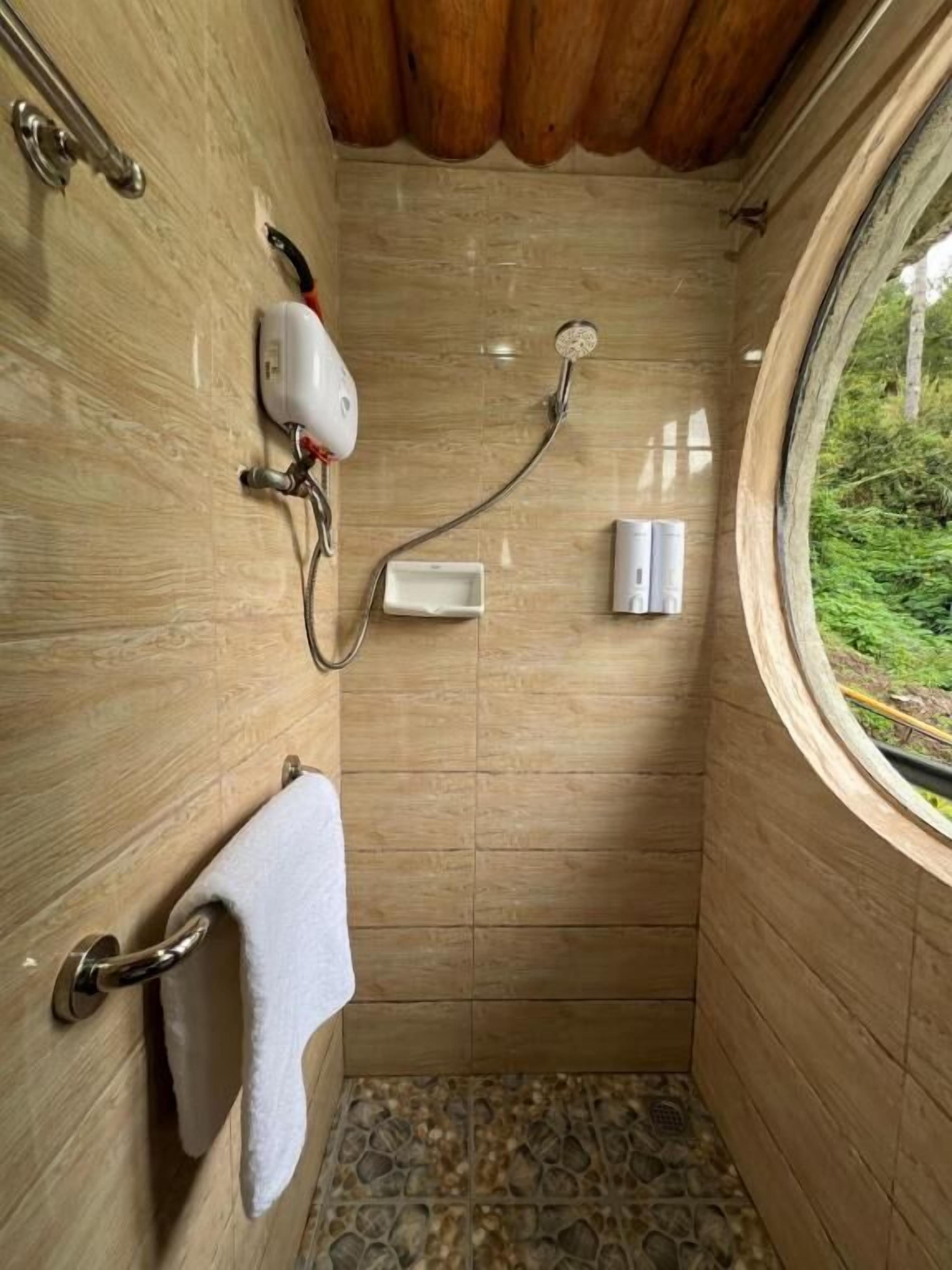 A small, wooden-walled shower with a window, a towel rack, and a handheld showerhead.
