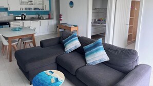 Un salon moderne avec un canapé gris, une table à manger et un coin cuisine à l’arrière-plan.