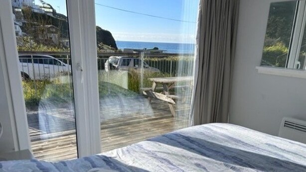 Une chambre à coucher avec un lit, un coussin en forme d’étoile de mer et une vue sur la mer et les véhicules qui passent.