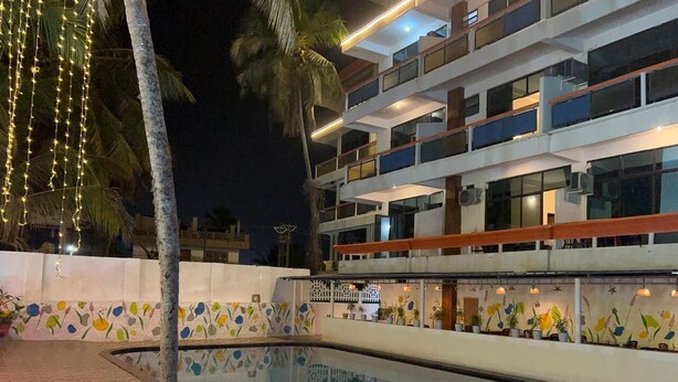 Una piscina con plataforma de cerámica, rodeada por un edificio de varios pisos con balcones y un muro decorativo con motivos florales.