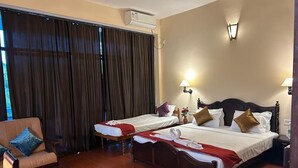 Habitación de hotel con dos camas, un sofá, una ventana con cortinas, un aire acondicionado instalado en la pared y dos lámparas de pared.
