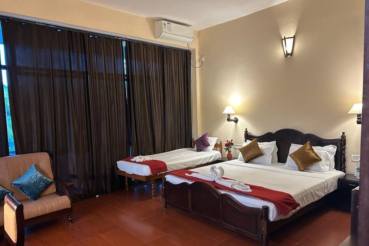 A hotel room with two beds, a sofa, a window with curtains, a wall-mounted air conditioner, and two wall lamps.