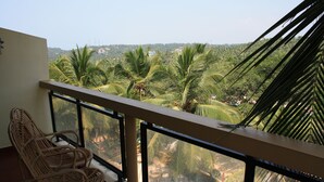 Un balcón con sillones de mimbre, barandilla de vidrio y vistas a palmeras y edificios a lo lejos.