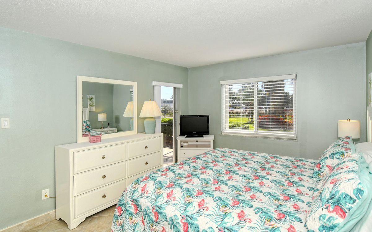 A bedroom with a bed, dresser, TV, and window with blinds.
