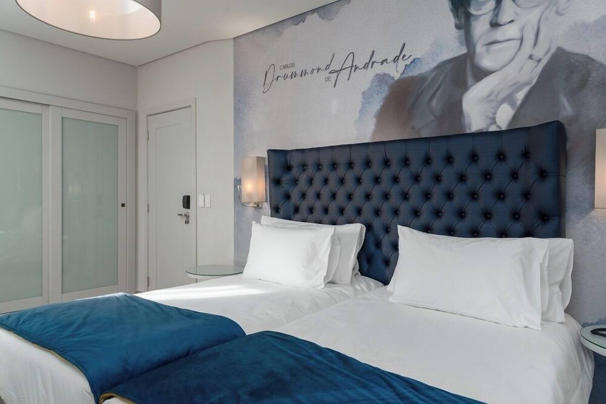 Hotelkamer met een groot bed, een gestapeld hoofdbord, wit beddengoed en een muur met een portret en tekst.