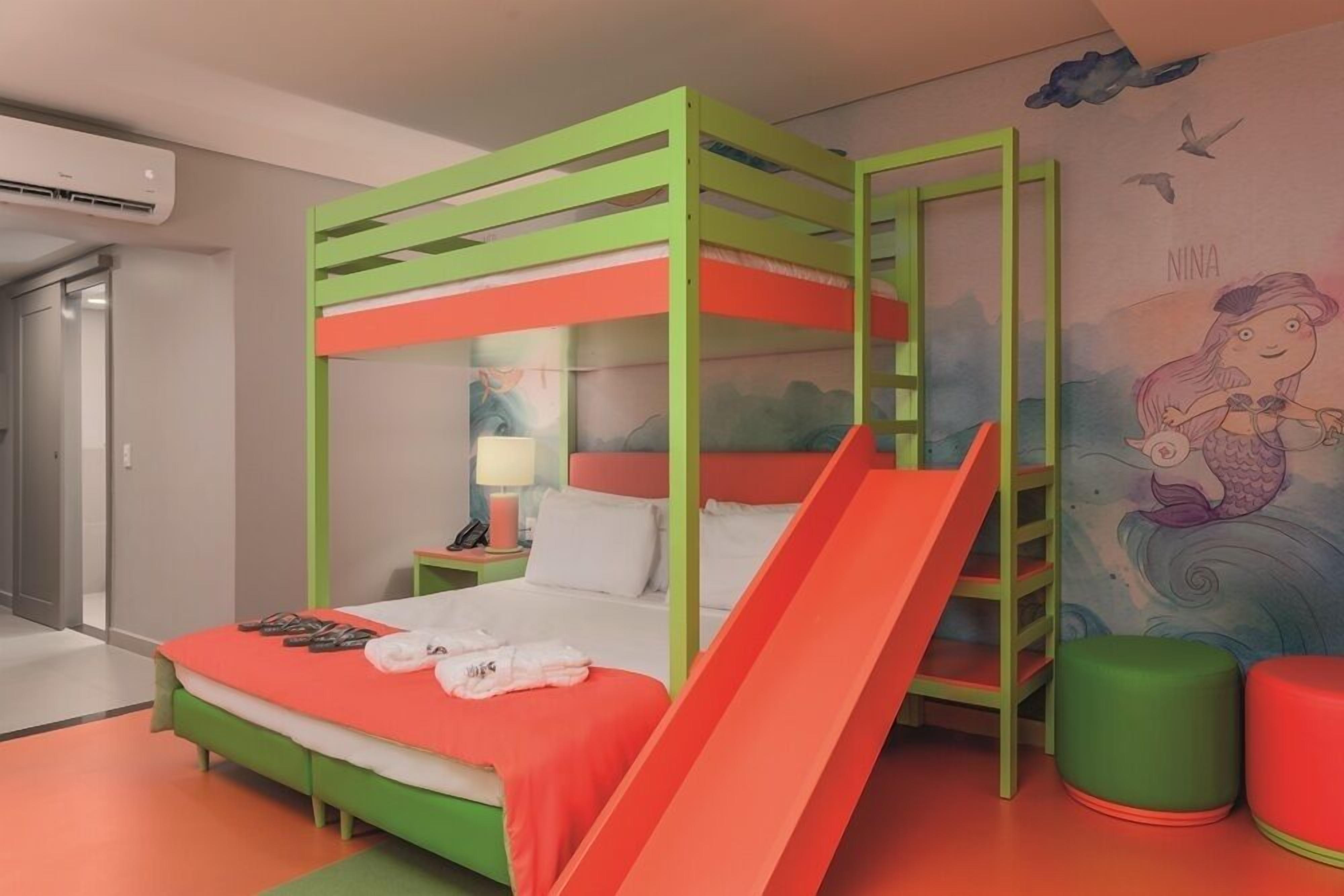 A colorful children's room with a bunk bed, a slide, and a mural of a mermaid.
